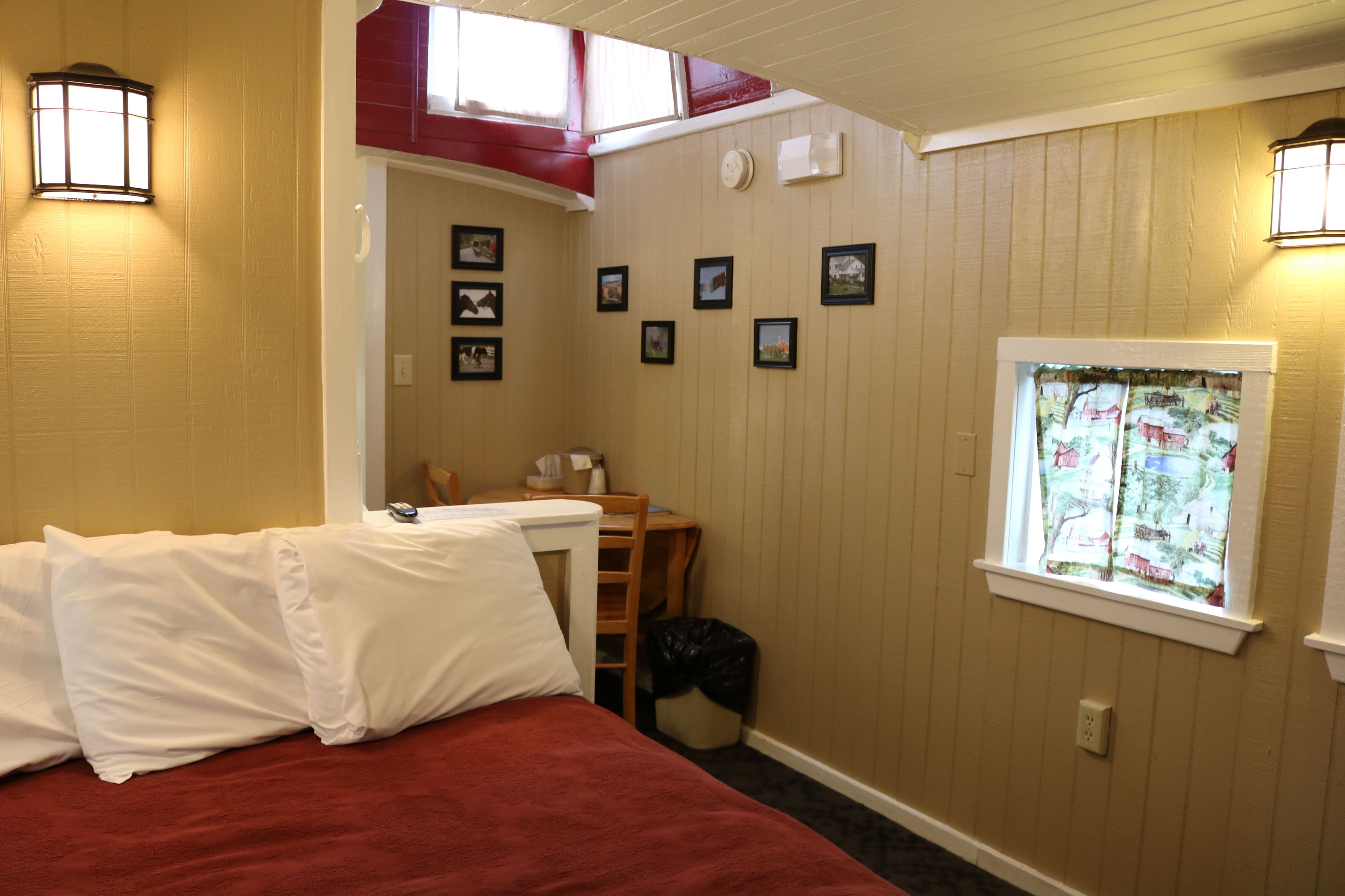 A bedroom with a bed, a desk, and a window with curtains.