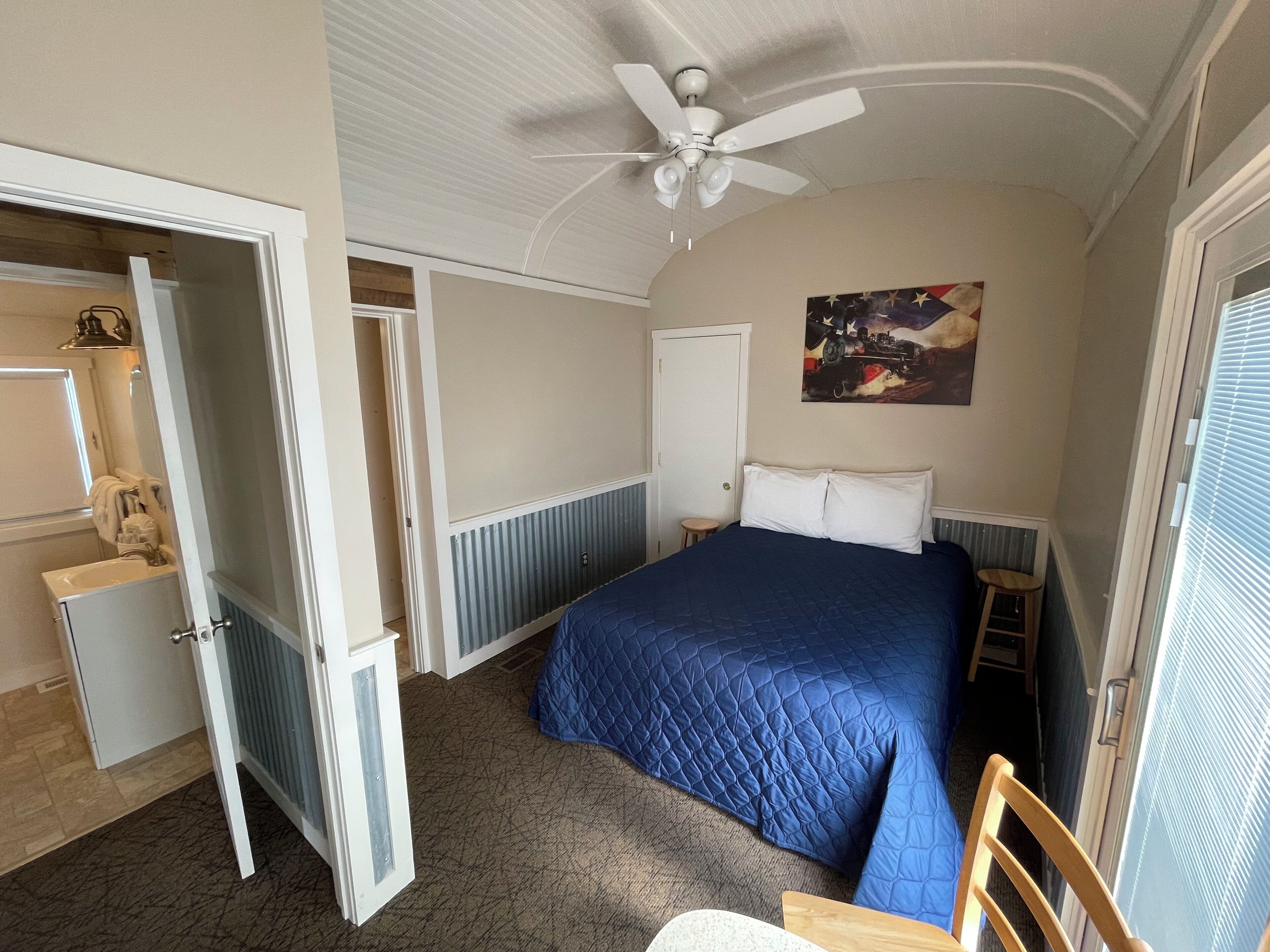A bedroom with a bed, a ceiling fan, a nightstand, a chair, and a painting on the wall.