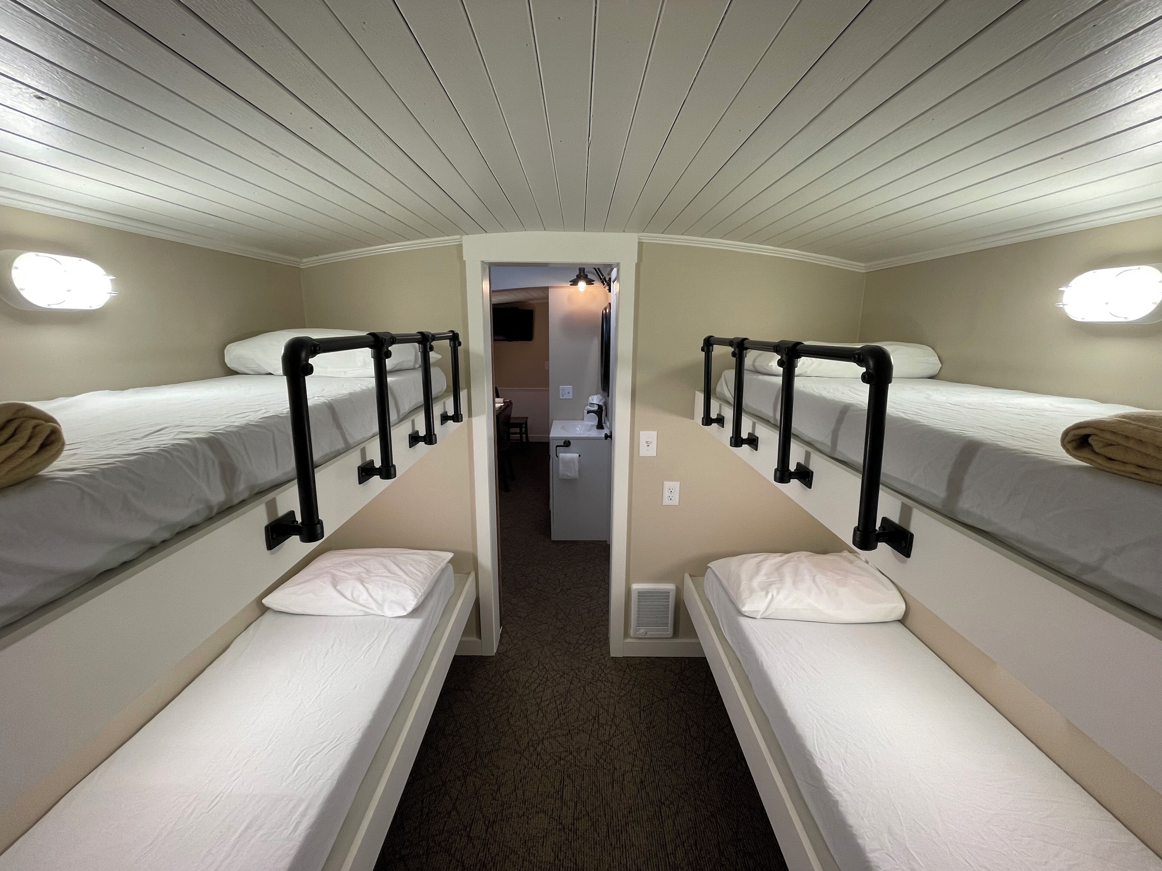 A narrow, well-lit room with bunk beds, a small kitchenette, and a bathroom.