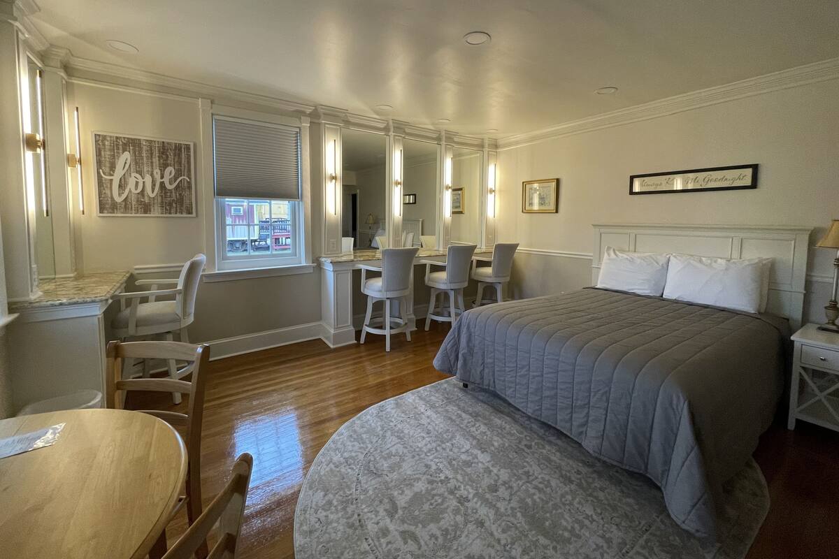 A bedroom with a bed, a desk, two chairs, a round table, and a window with blinds.