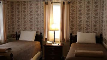 Une chambre avec deux lits, un papier peint à motifs floraux, une table de chevet avec une lampe et une fenêtre avec des rideaux.