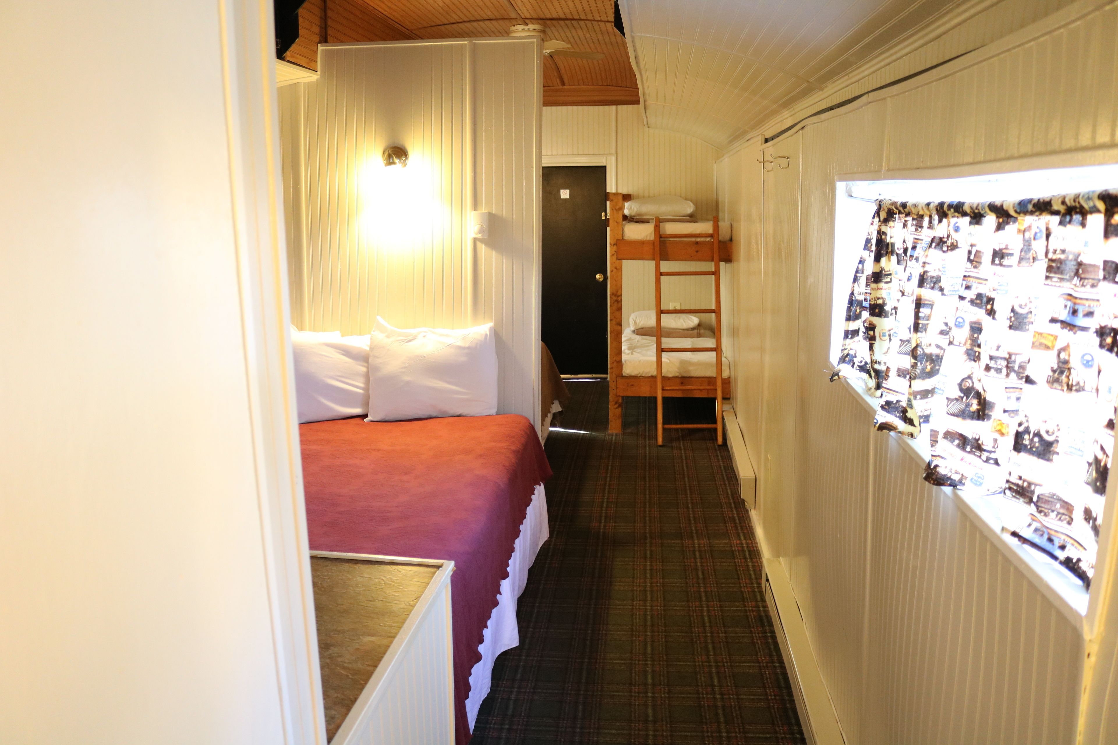 A narrow corridor with a bunk bed on the left and a window with a curtain on the right.