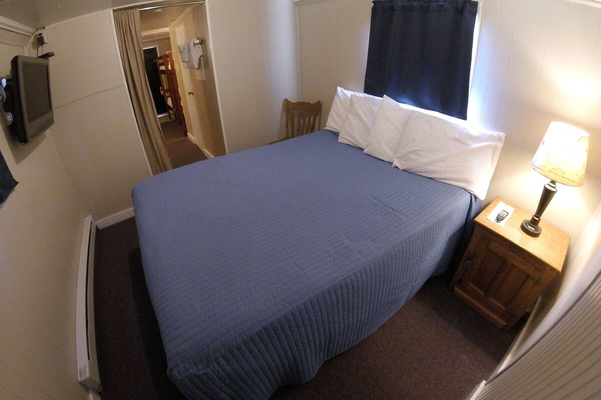 A hotel room with a bed, a nightstand with a lamp, and a TV mounted on the wall.