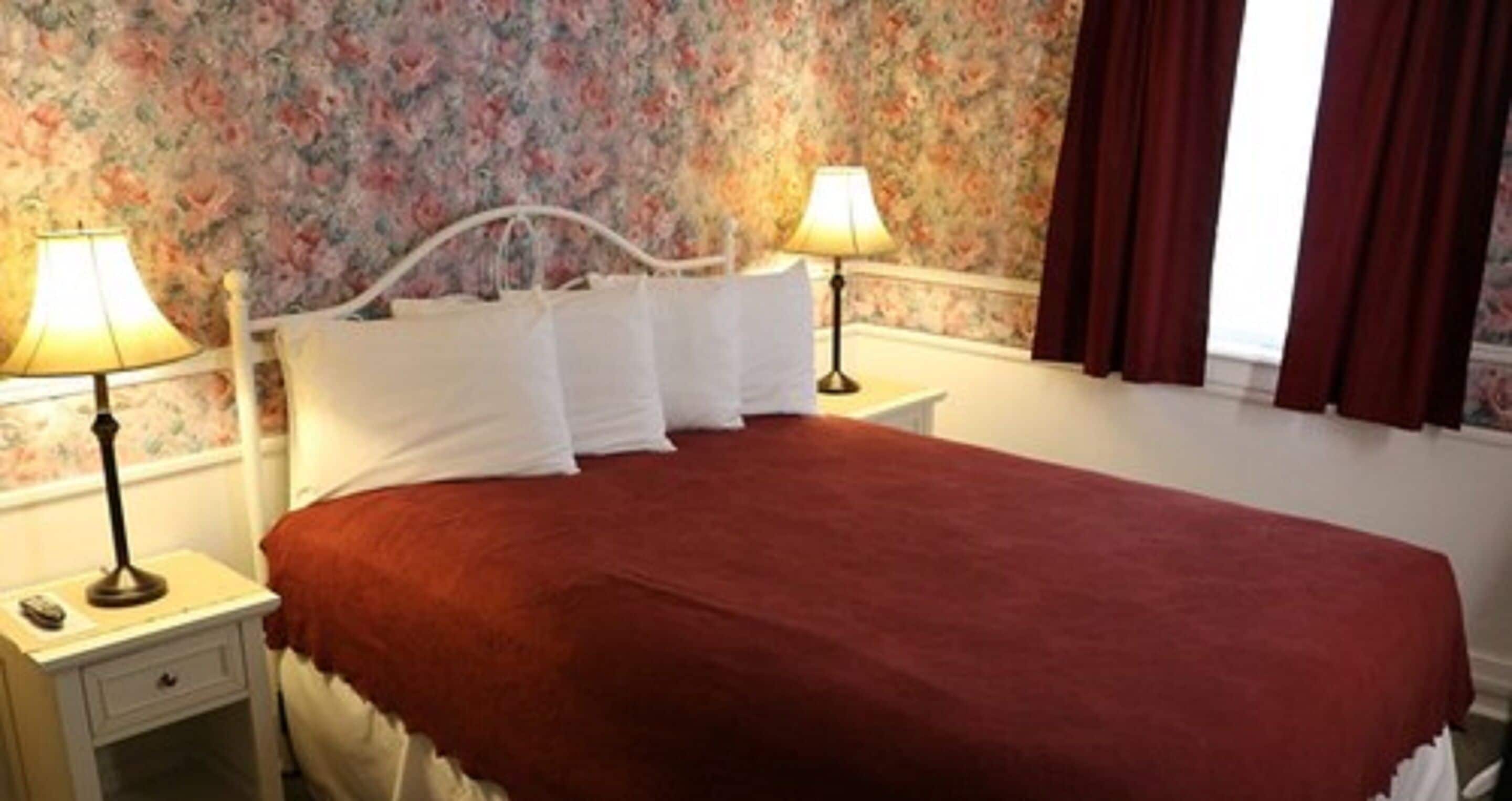 A bed with white linens, two bedside lamps, and a floral wallpaper background.
