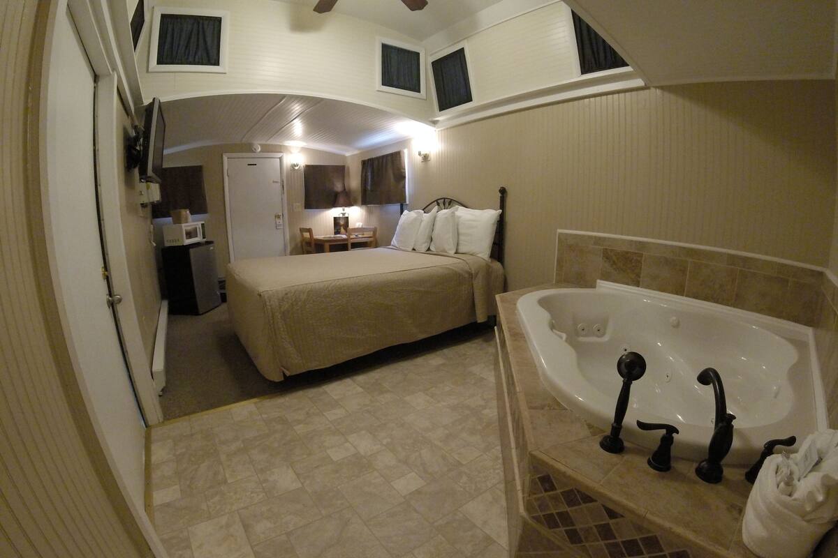 A hotel room with a bed, a bathroom with a bathtub, and a desk with a chair.