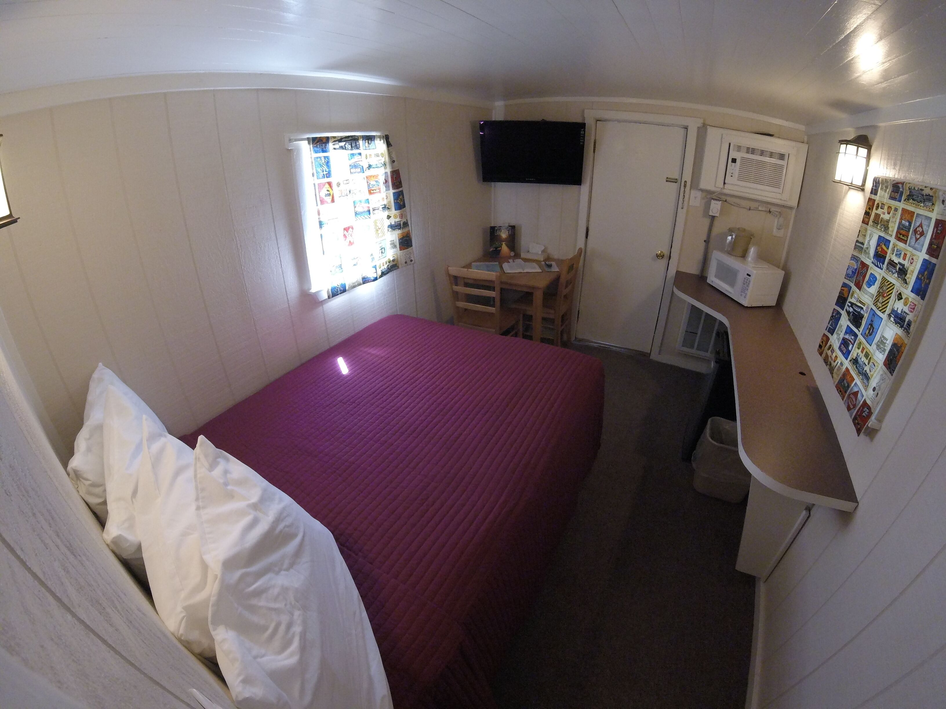 A compact room with a bed, a small desk, a television, and a microwave.