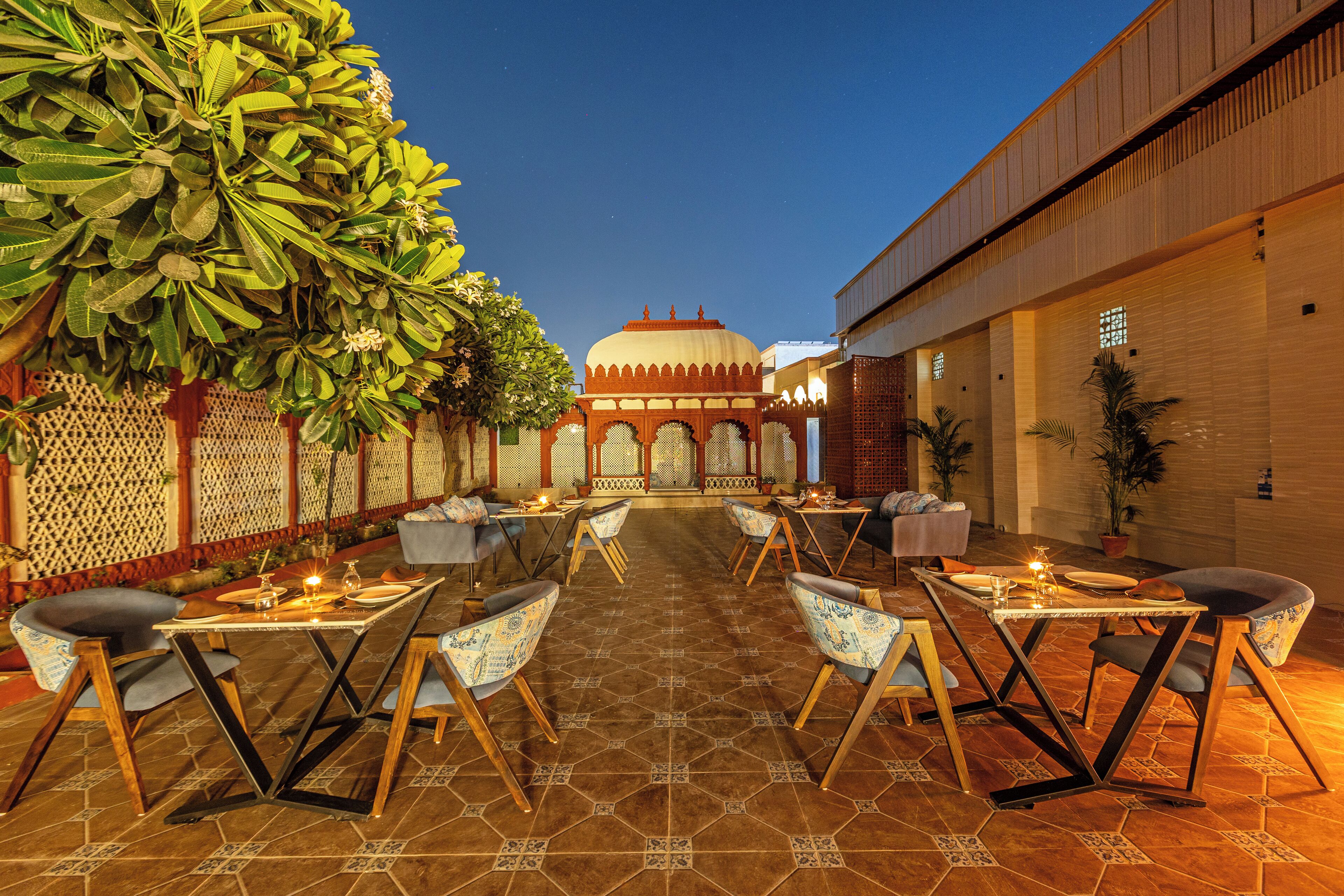 An outdoor dining area with tables and chairs, a decorative fence, and a building with a dome in the background.