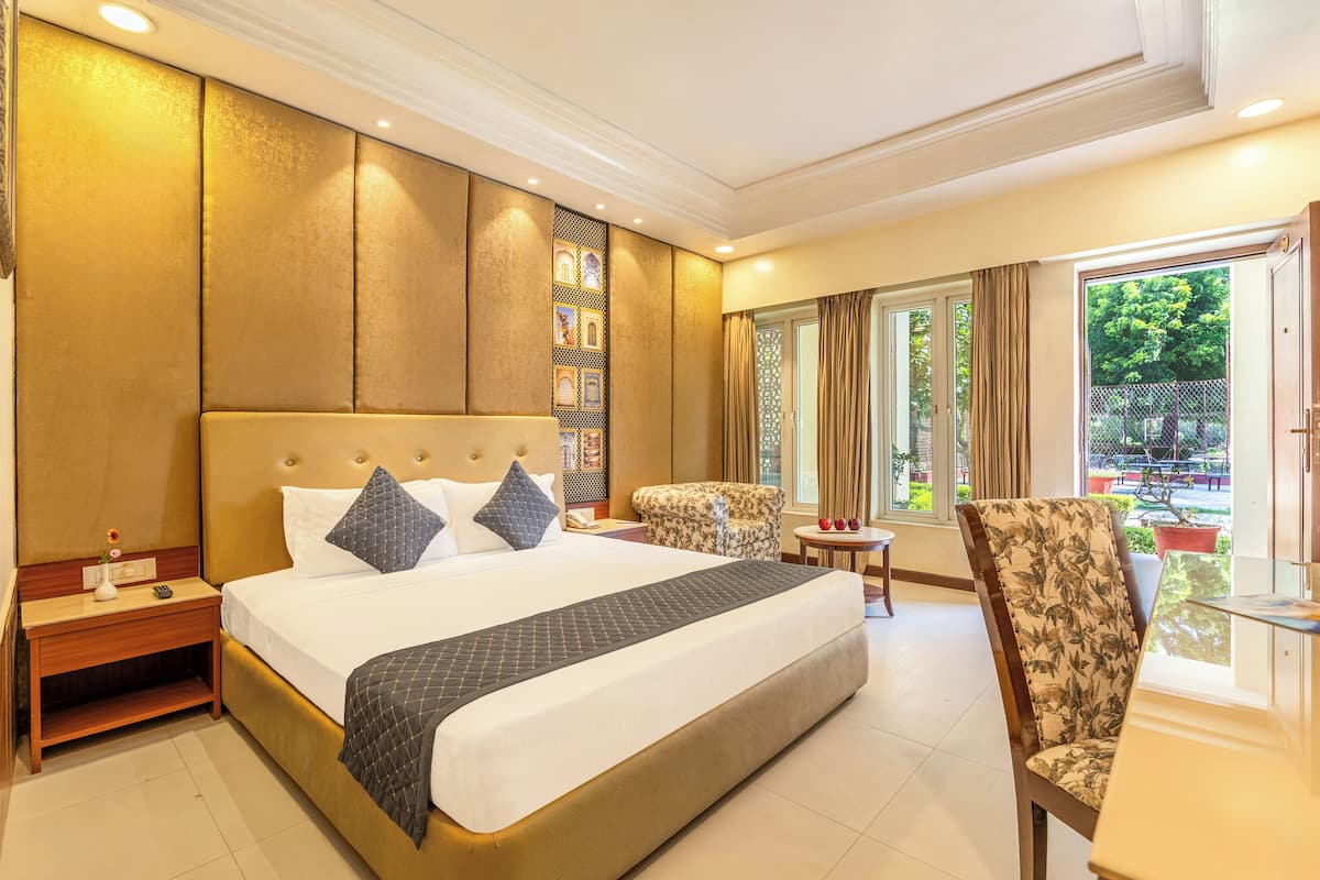 A hotel room with a large bed, a nightstand, a chair, a small table, and a window with curtains.