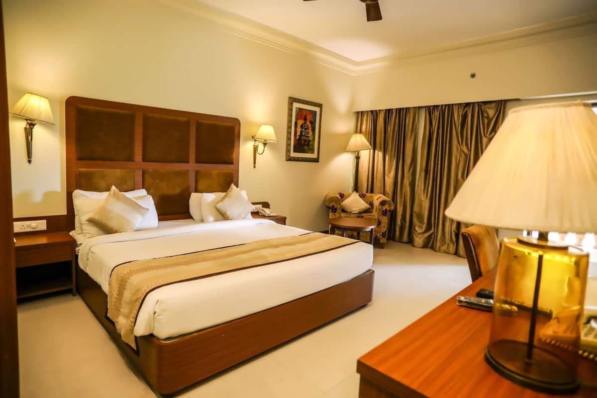A hotel room with a large bed, bedside tables, a chair, a desk, and a lamp.