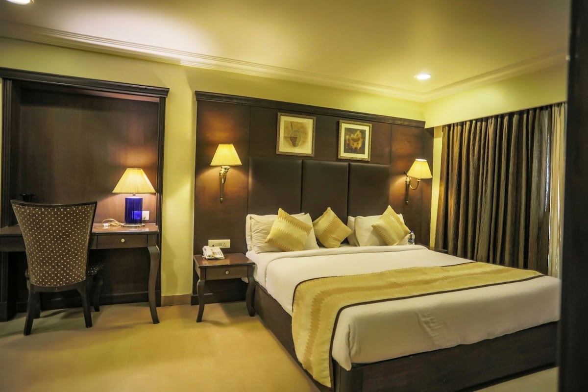 A hotel room with a bed, desk, chair, lamps, and a nightstand.