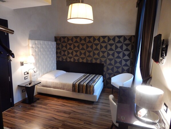 Una habitación de hotel con cama, mesita de noche, lámpara y cafetera.