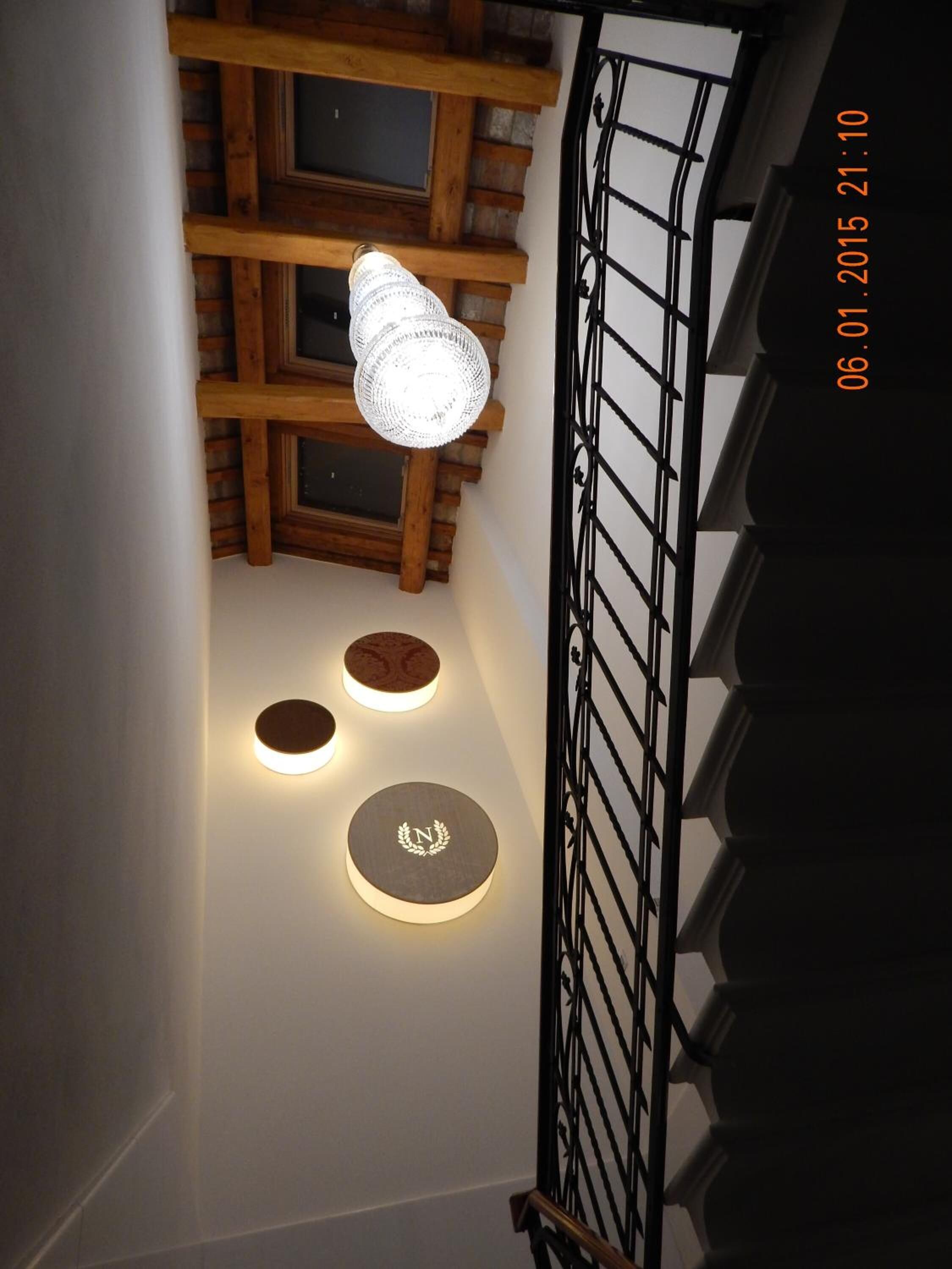 A staircase with a wooden handrail and a metal railing. There are three illuminated wall sconces with a circular design and a central emblem.