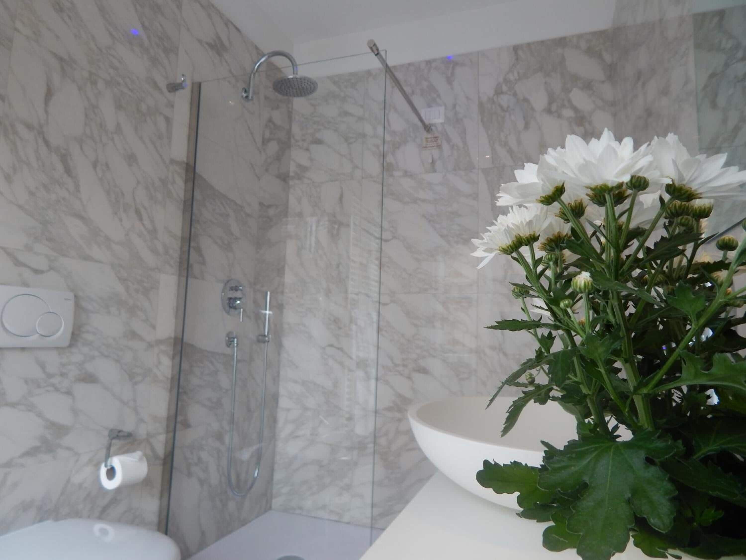A bathroom with a marble shower, a white sink, and a toilet.