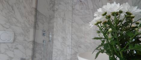 A bathroom with a marble shower, a white sink, and a toilet.