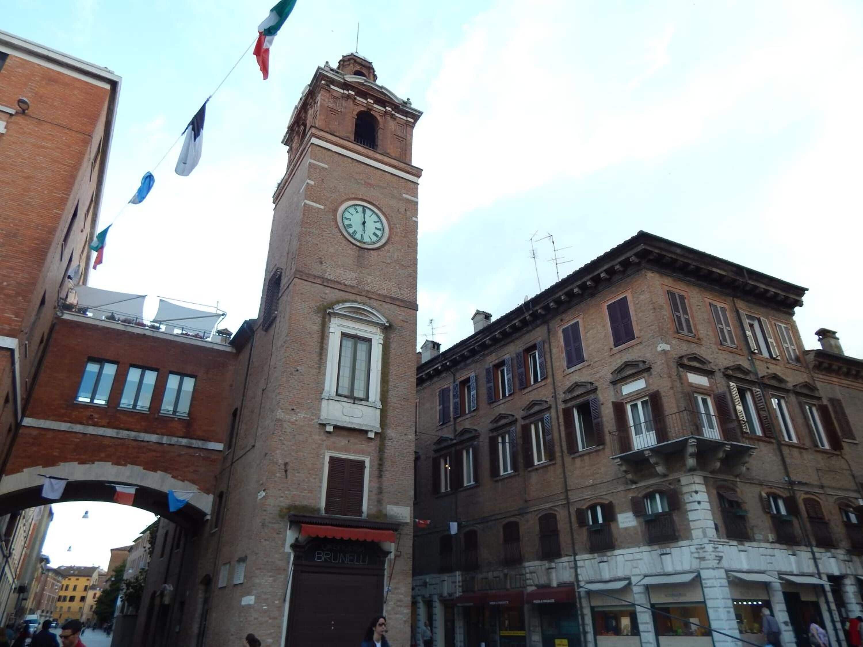 A historic building with a clock tower, a sign reading "BRUNELLI," and a street view with pedestrians.