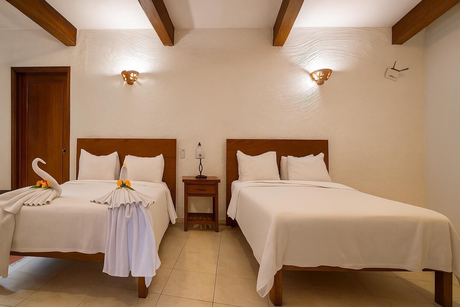 A hotel room with two beds, wooden headboards, a nightstand with a lamp, and a decorative swan on the left bed.