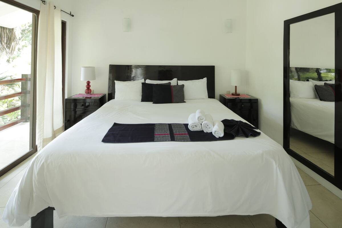 Hotelkamer met een groot bed, twee nachtkastjes, een spiegel en uitzicht op groen.