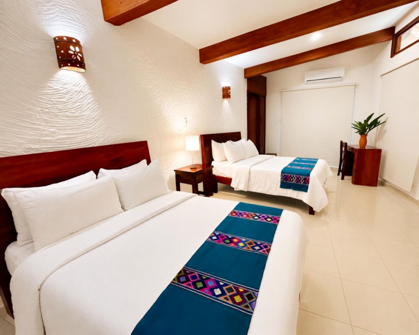 A hotel room with two beds, a wooden headboard, a nightstand, a lamp, a potted plant, and a wall-mounted air conditioning unit.