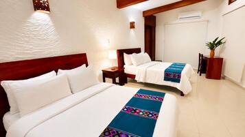 A hotel room with two beds, a wooden headboard, a nightstand, a lamp, a potted plant, and a wall-mounted air conditioning unit.