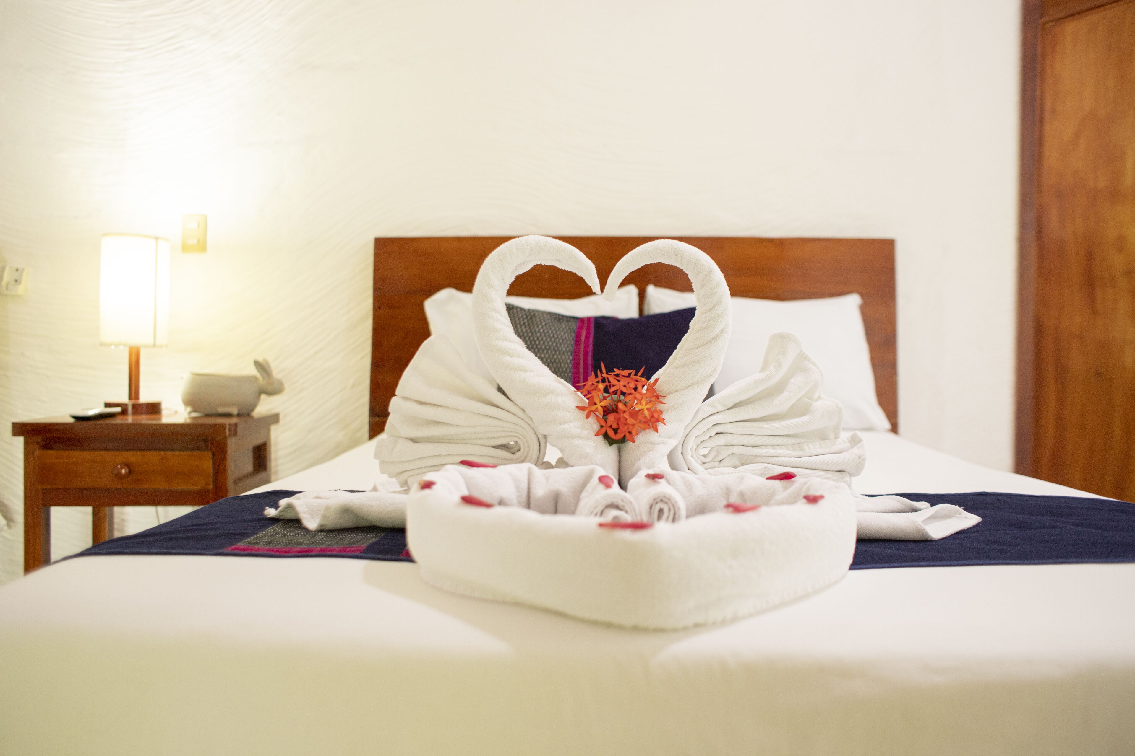 Una cama bien tendida con un arreglo de toallas con forma de corazón y un centro de mesa floral decorativo.