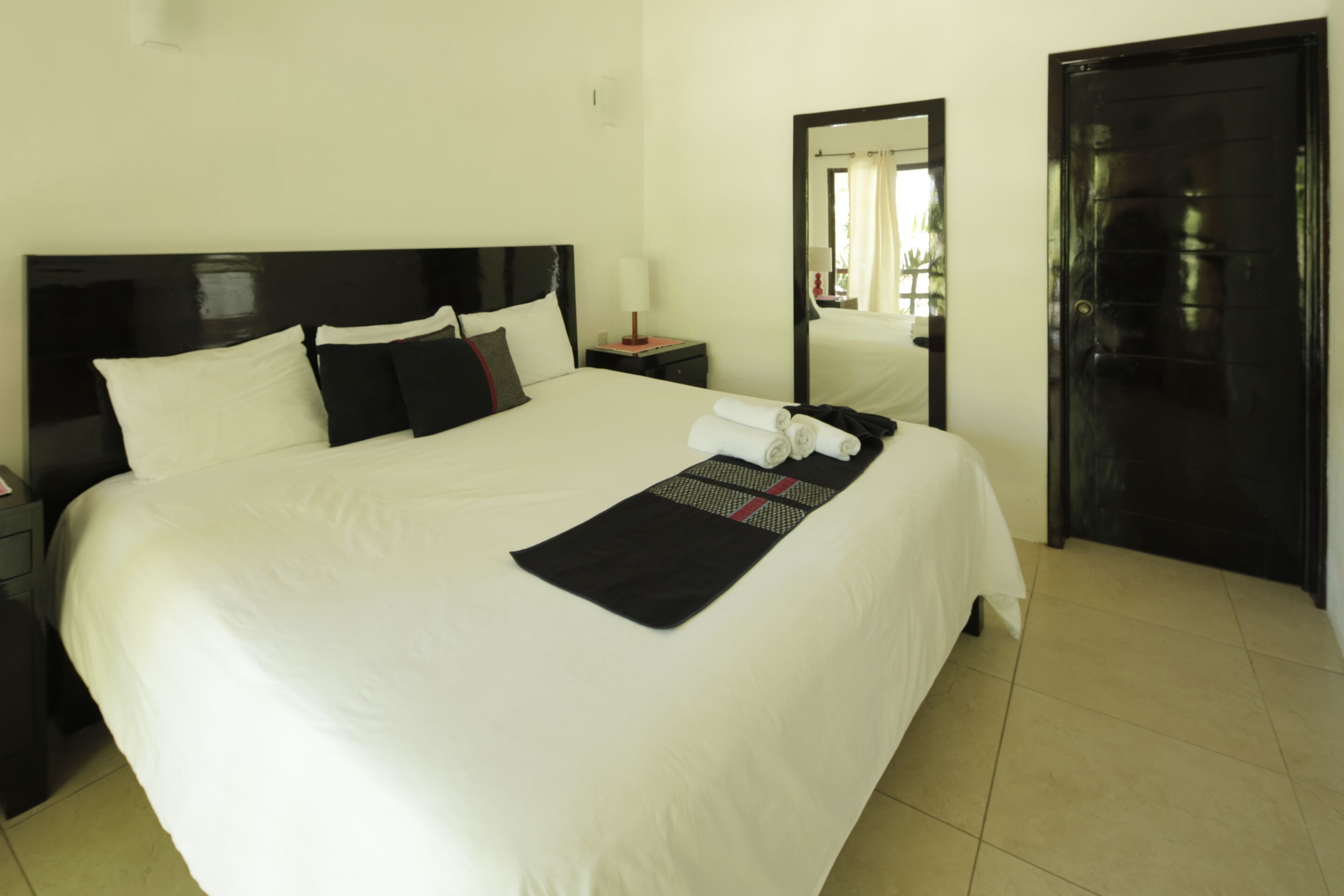 A neatly made bed with white linens, a black headboard, and a black runner with red accents.