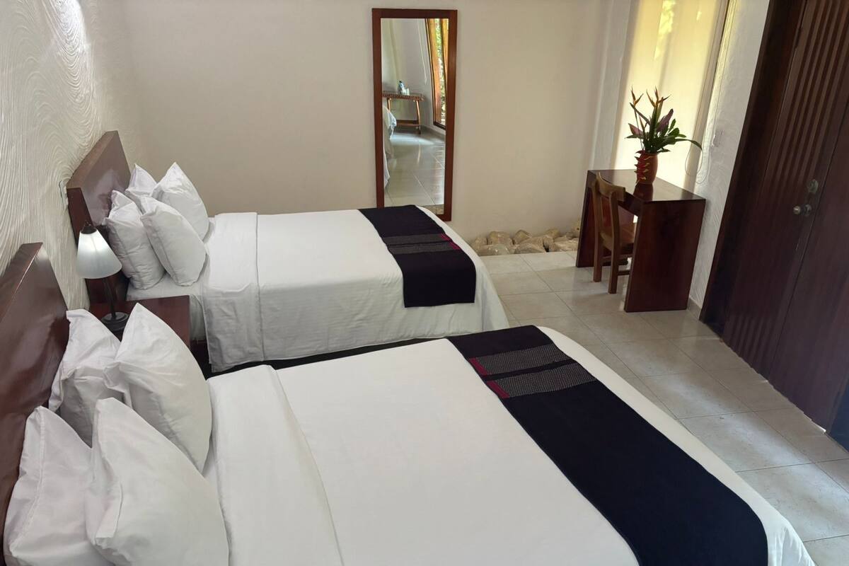 Een hotelkamer met twee bedden, een houten hoofdbord, een klein tafeltje met een plant en een spiegel aan de muur.