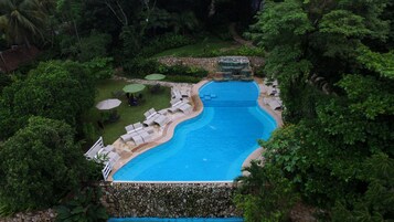 Una piscina de borde curvo, rodeada de abundante vegetación y un muro de piedra.