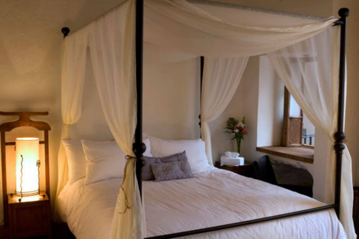 Ein Bett mit Baldachin, ausgestattet mit weißer Bettwäsche, ein Nachttisch mit Lampe und ein Spiegel an der Wand.