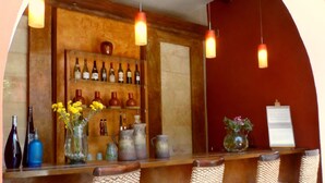 Un espace bar avec des fauteuils en osier, un présentoir à vin et des lampes suspendues.