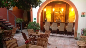 Un espace extérieur aménagé en terrasse, avec des tables et des chaises en bois, un bar avec des bouteilles et un escalier menant à un niveau supérieur.