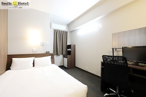 A hotel room with a bed, a desk, a chair, a TV, an air conditioner, and a small cabinet.
