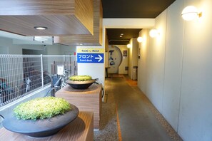 A hotel corridor with a directional sign to the front desk, a reception area, and a wall-mounted sign with the hotel's name.