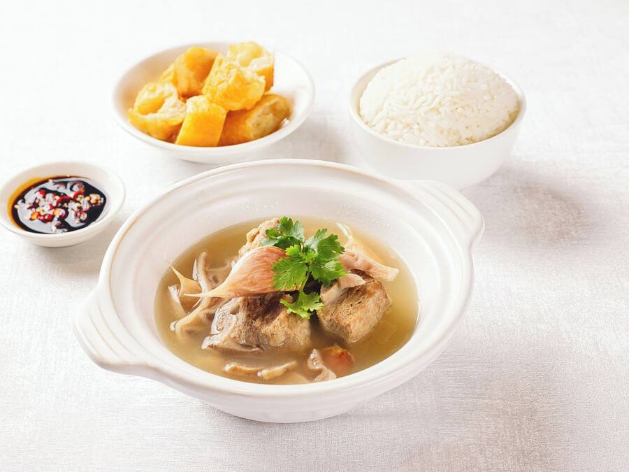 A bowl of soup with meat and vegetables, accompanied by a bowl of rice, a small bowl of sauce, and a dish of what appears to be tofu.