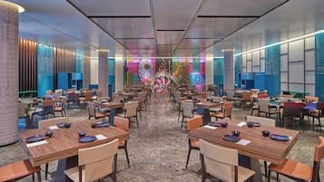 Un amplio vestíbulo de hotel con varias mesas y sillas de comedor, una pared decorativa central y un diseño de techo moderno.