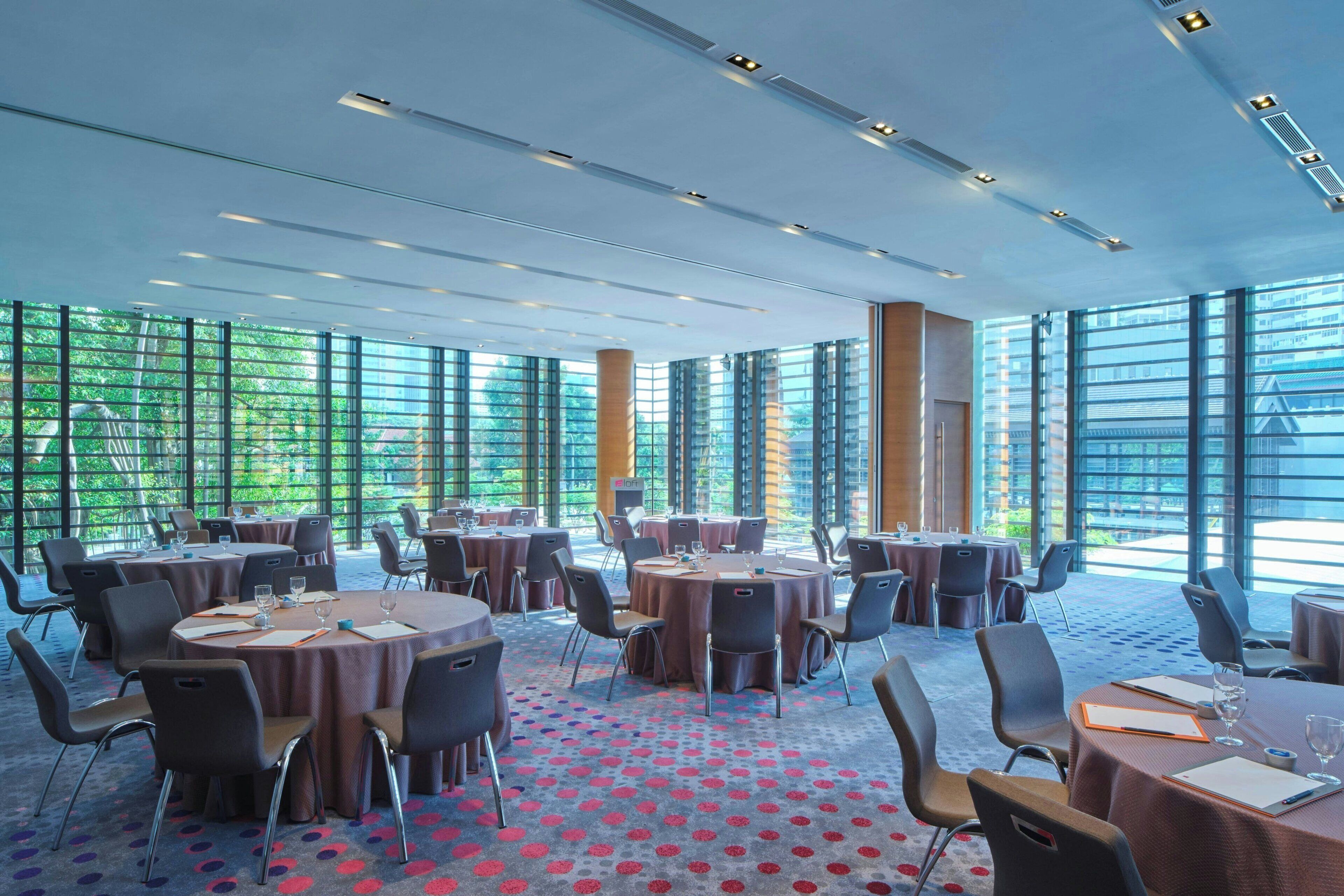 A spacious conference room with round tables, chairs, and a carpeted floor.