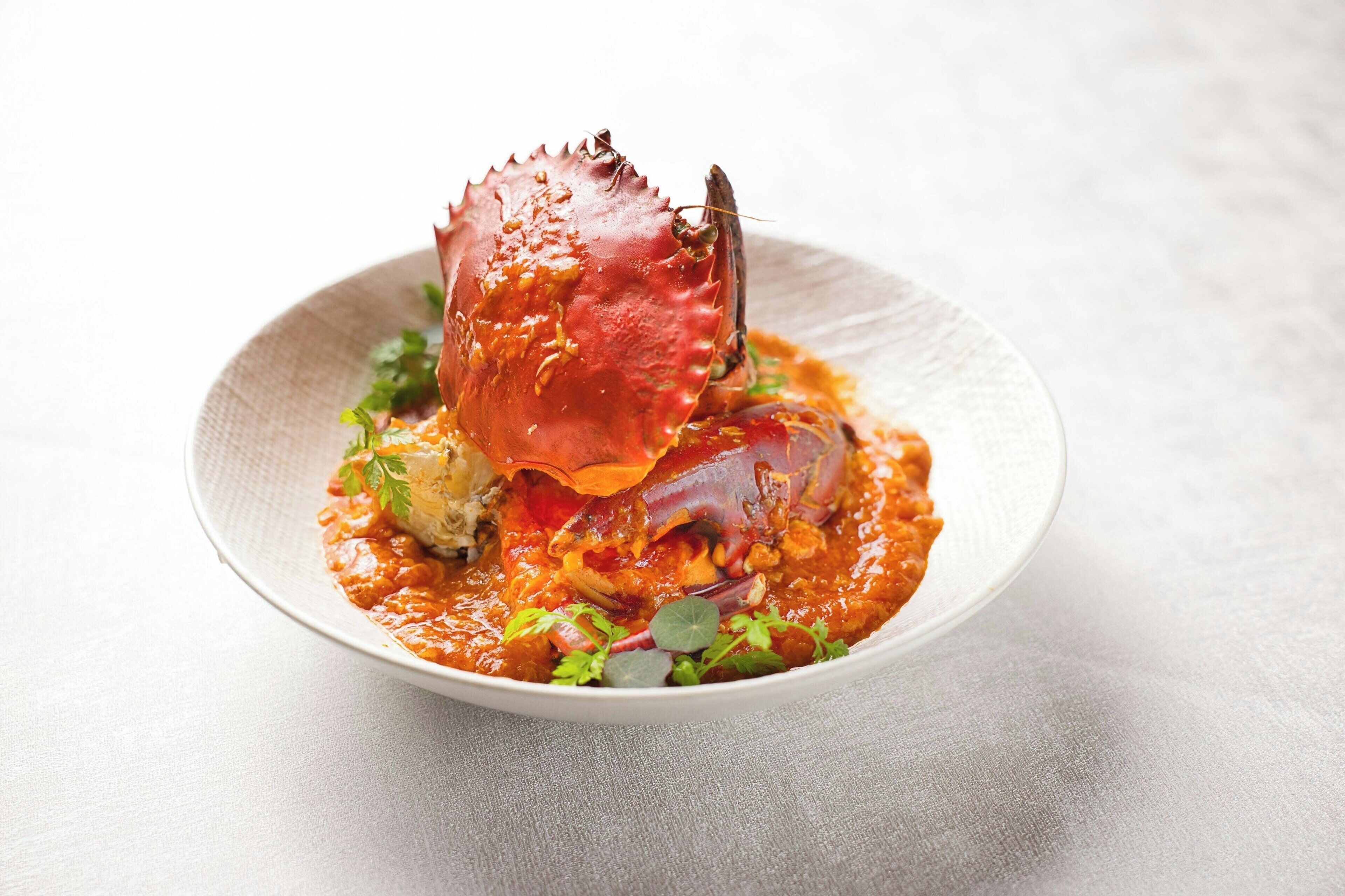 Un plato con un cangrejo cocido y salsa, adornado con hierbas.