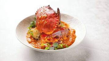 Un plato con un cangrejo cocido y salsa, adornado con hierbas.