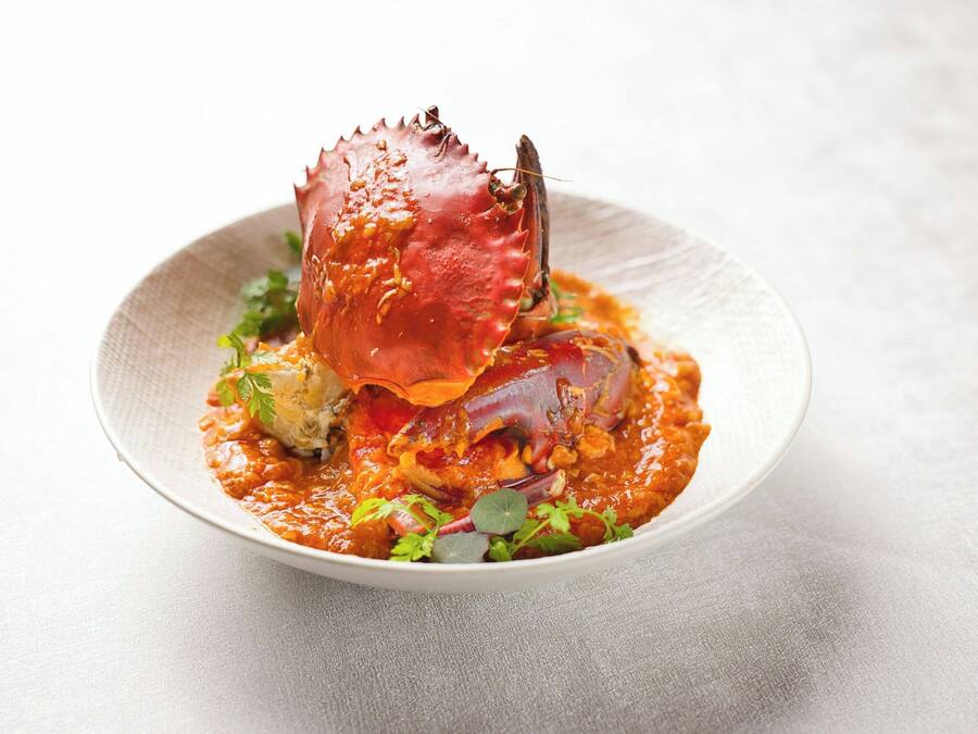 Un plato con un cangrejo cocido y salsa, adornado con hierbas.