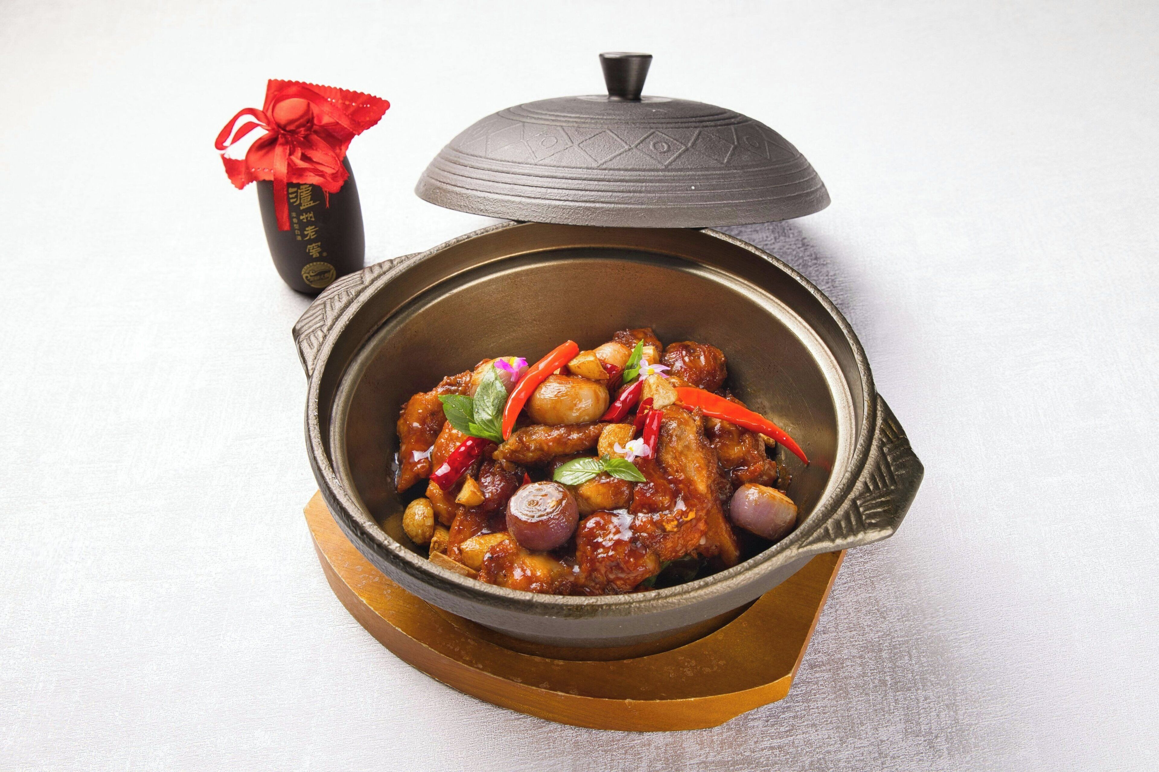 Una olla de barro tradicional con tapa, que contiene un guiso de carne, verduras y chiles rojos.