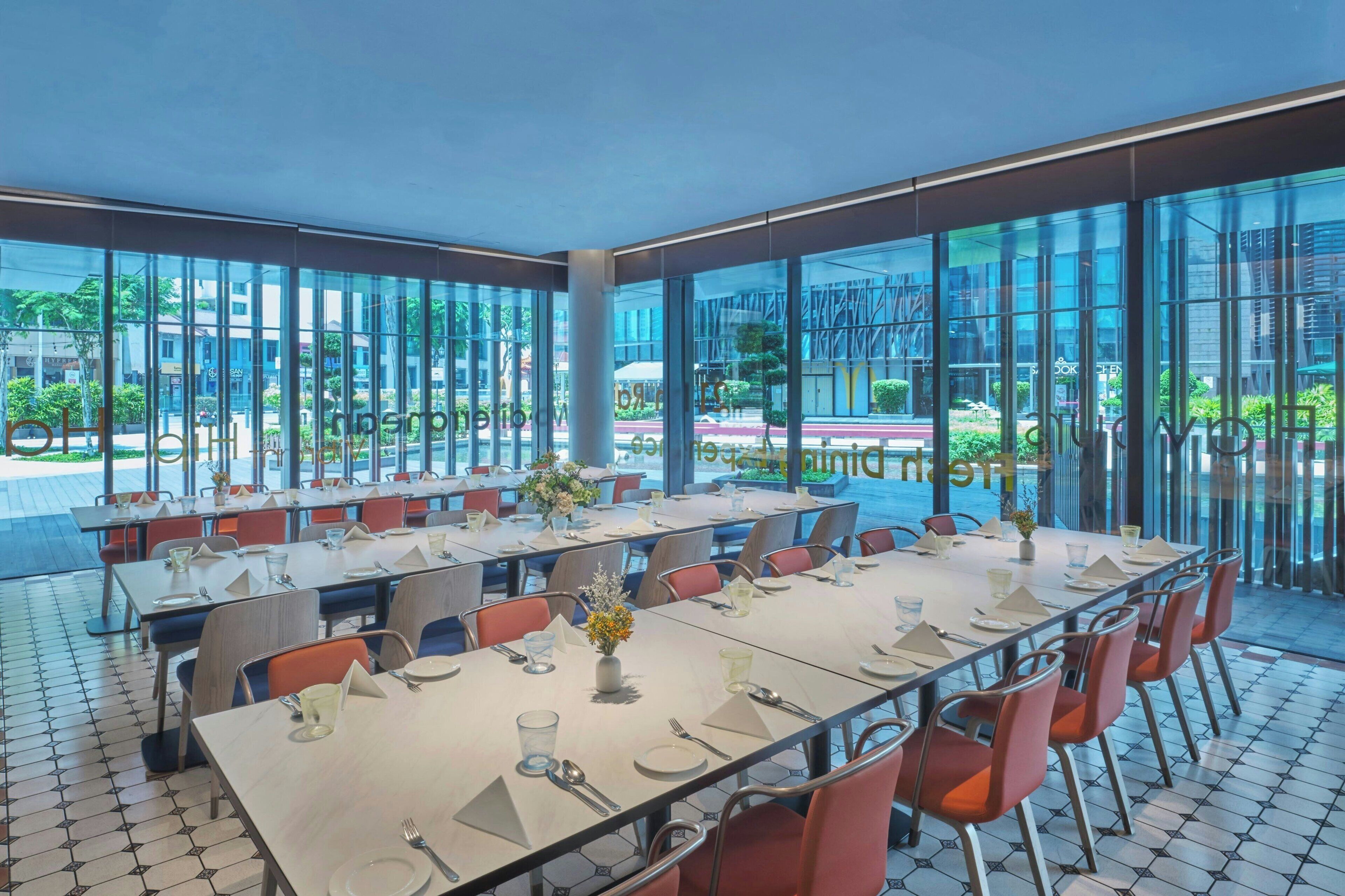 Un espace de restauration moderne doté de grandes fenêtres, de plusieurs tables dressées et offrant une vue sur l’extérieur.