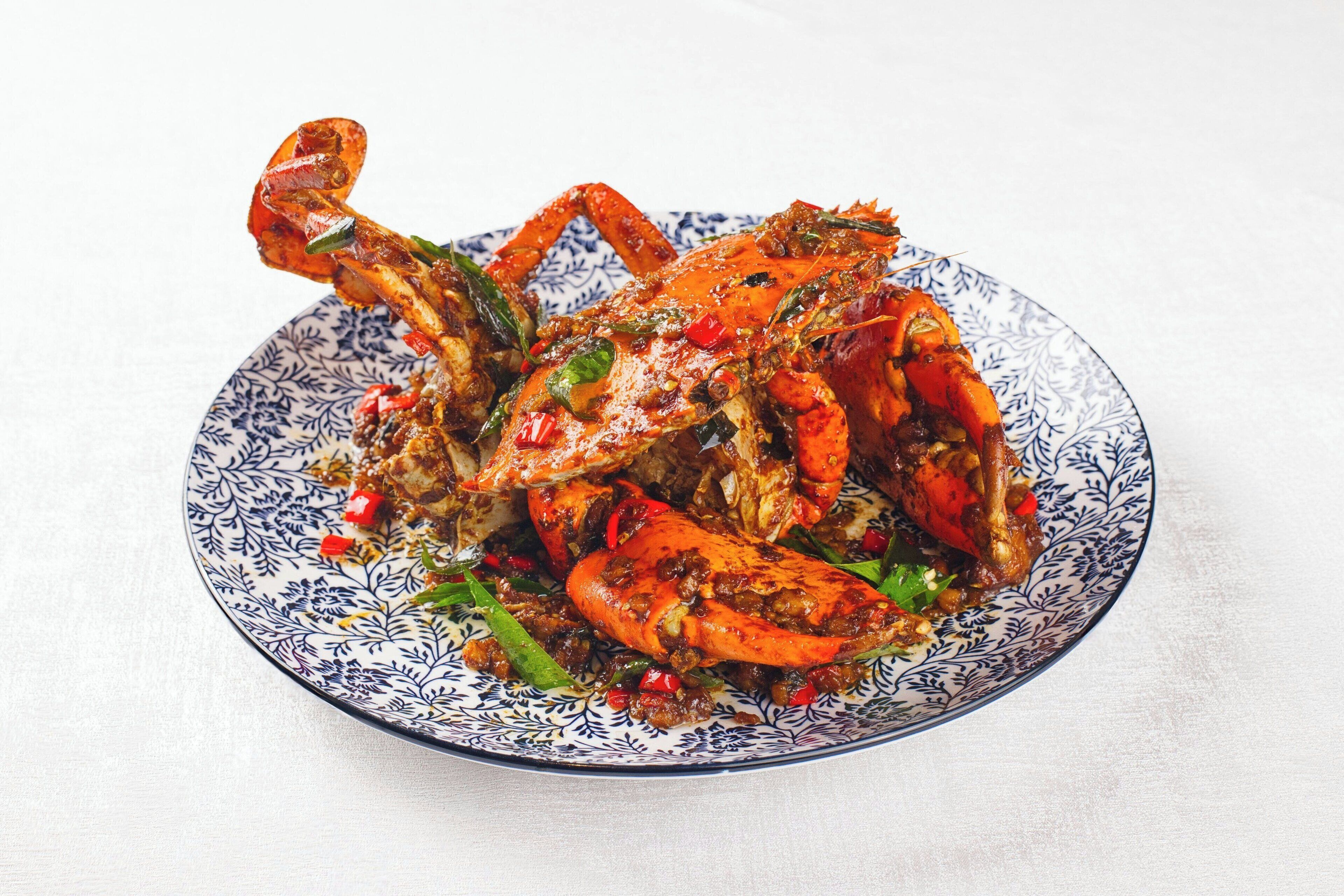A plate of cooked crab with red chili and green herbs.