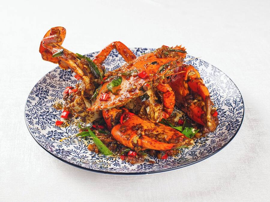 A plate of cooked crab with red chili and green herbs.