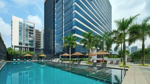 Un hotel moderno con una gran piscina, palmeras y edificios altos al fondo.