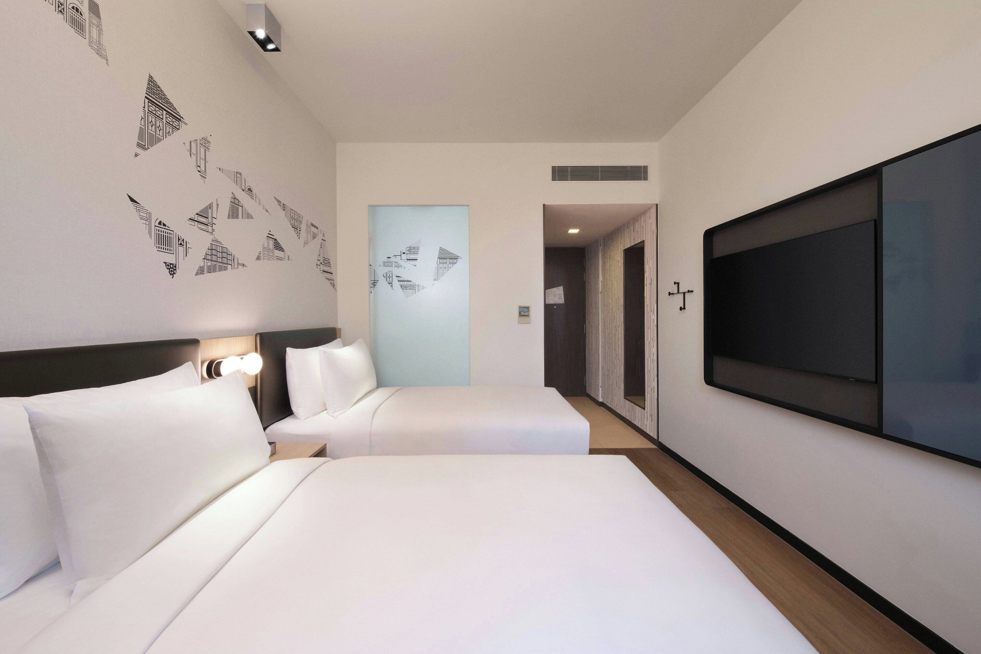 Habitación de hotel con dos camas, un televisor de pantalla plana grande y una pared decorada con arte geométrico.