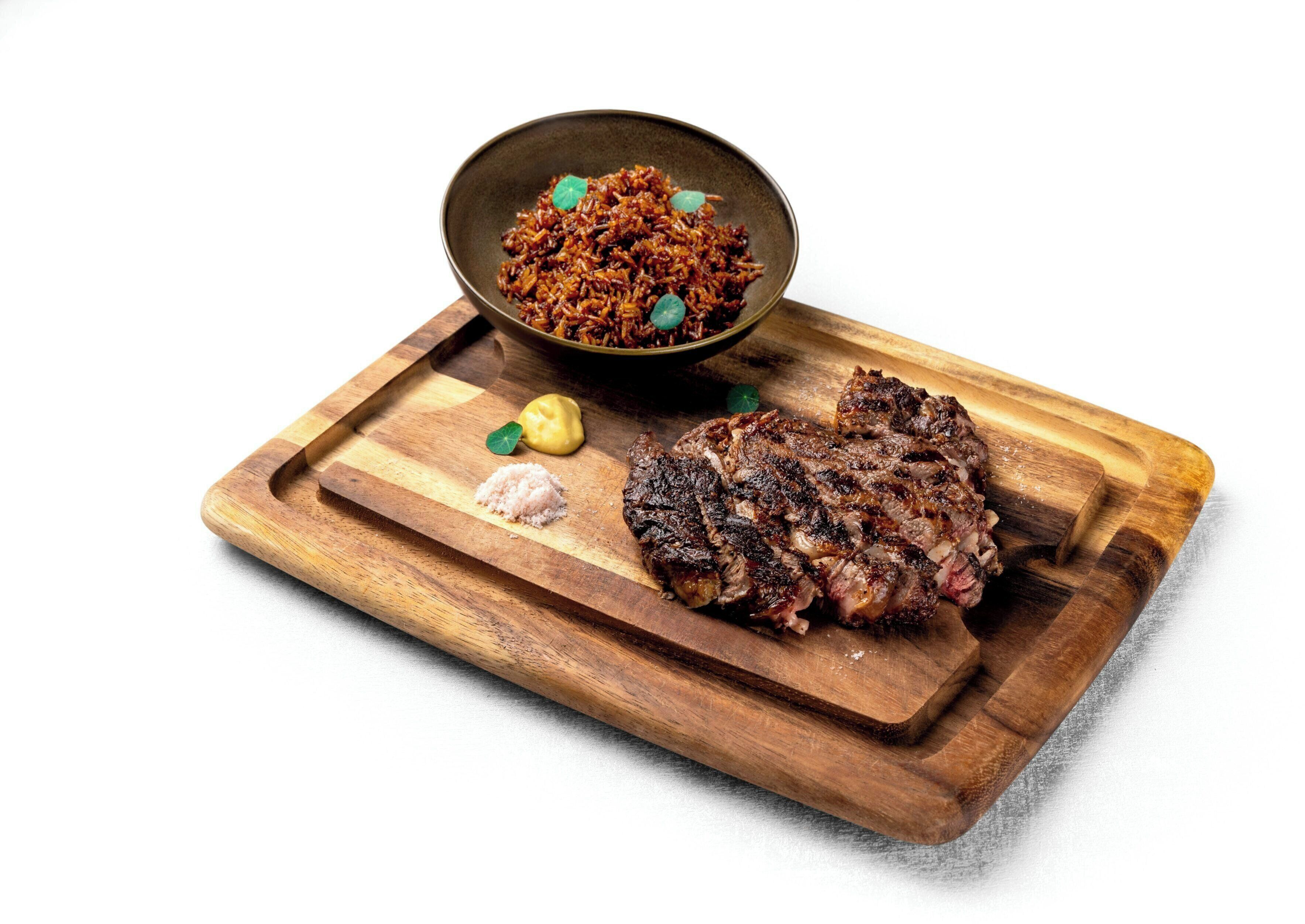 Ein Steak mit Reis und einer kleinen Schale Sauce auf einem Holzboden.