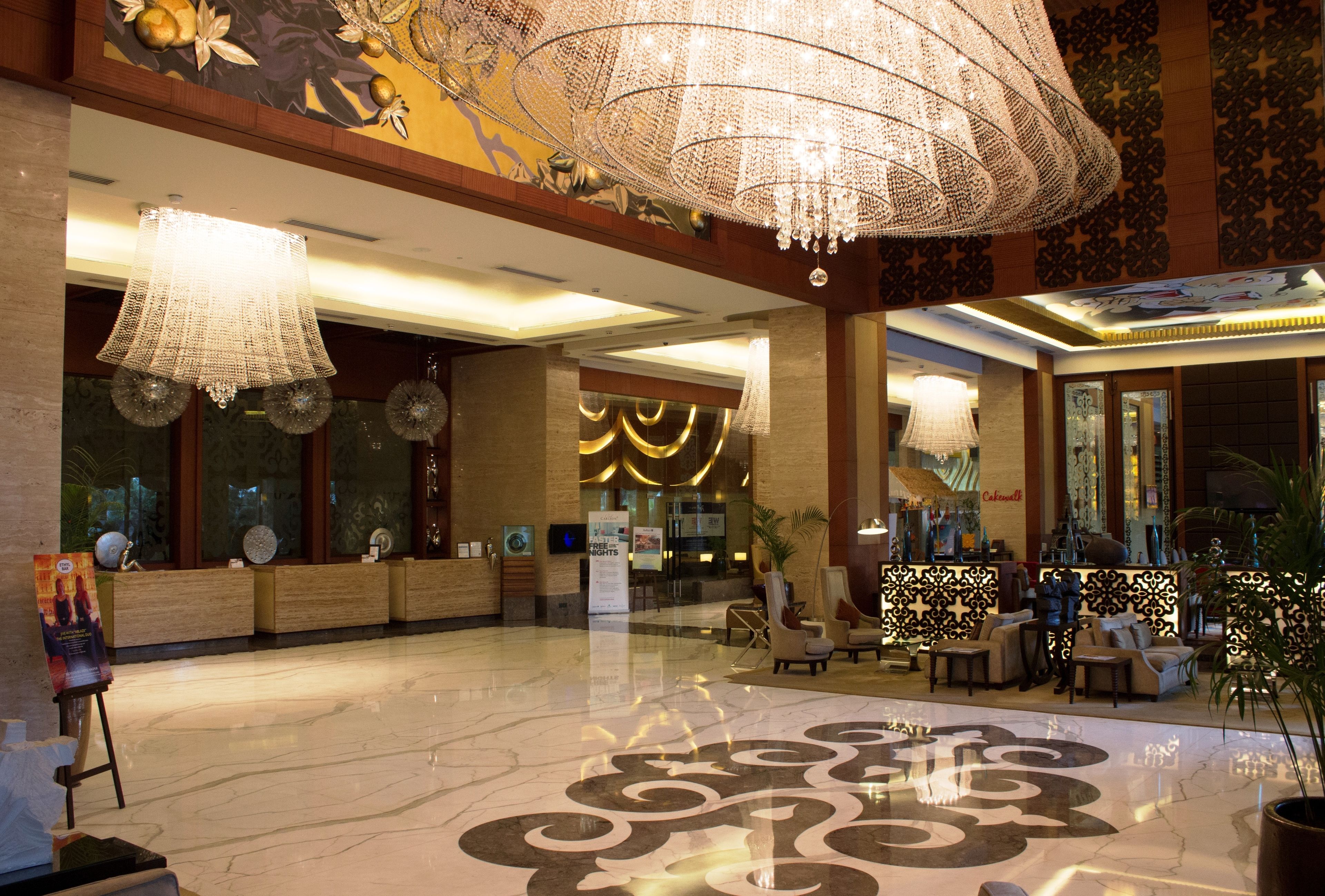 A spacious lobby with a high ceiling, chandeliers, and a reception desk.