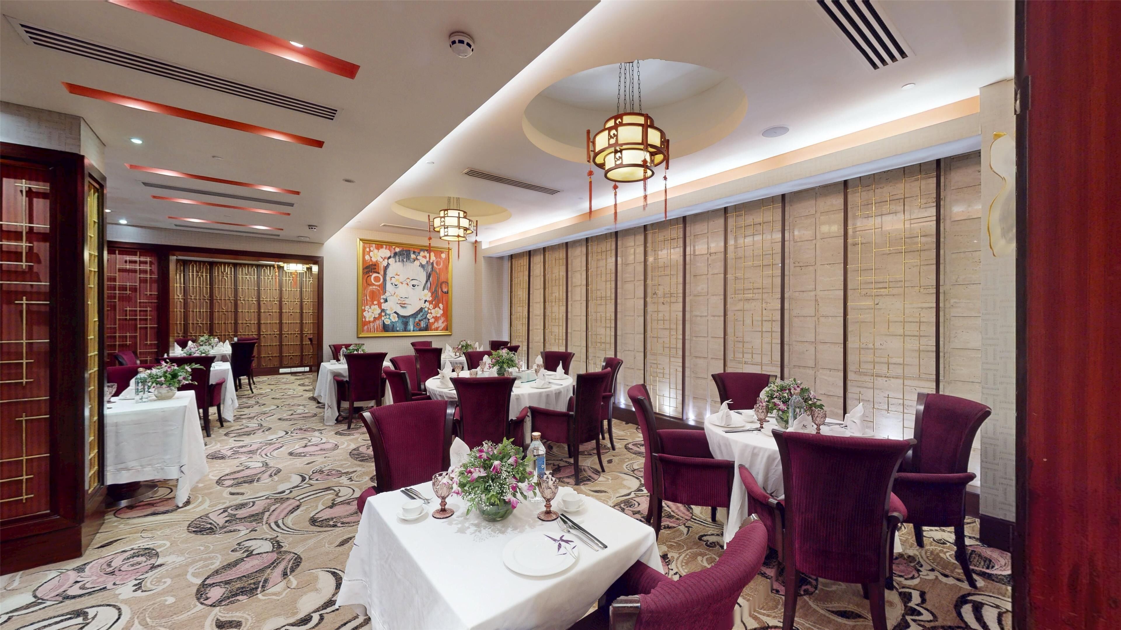 Un comedor de hotel con mesas redondas, sillas tapizadas en rojo y una alfombra estampada.
