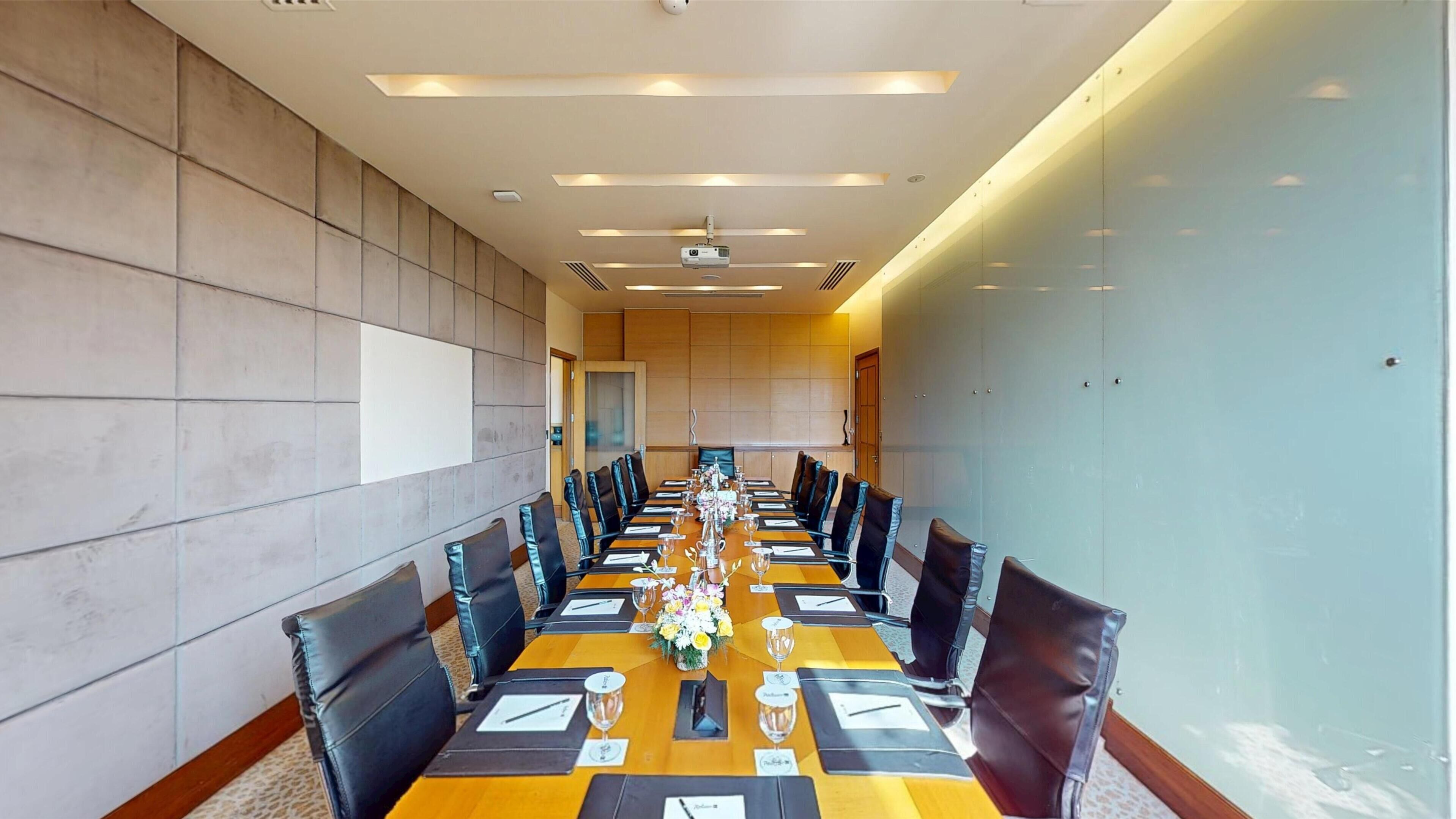 A conference room with a long table, black leather chairs, and a projector screen.