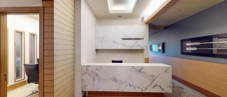 A modern reception area with a marble counter, wooden accents, and a ceiling with recessed lighting.