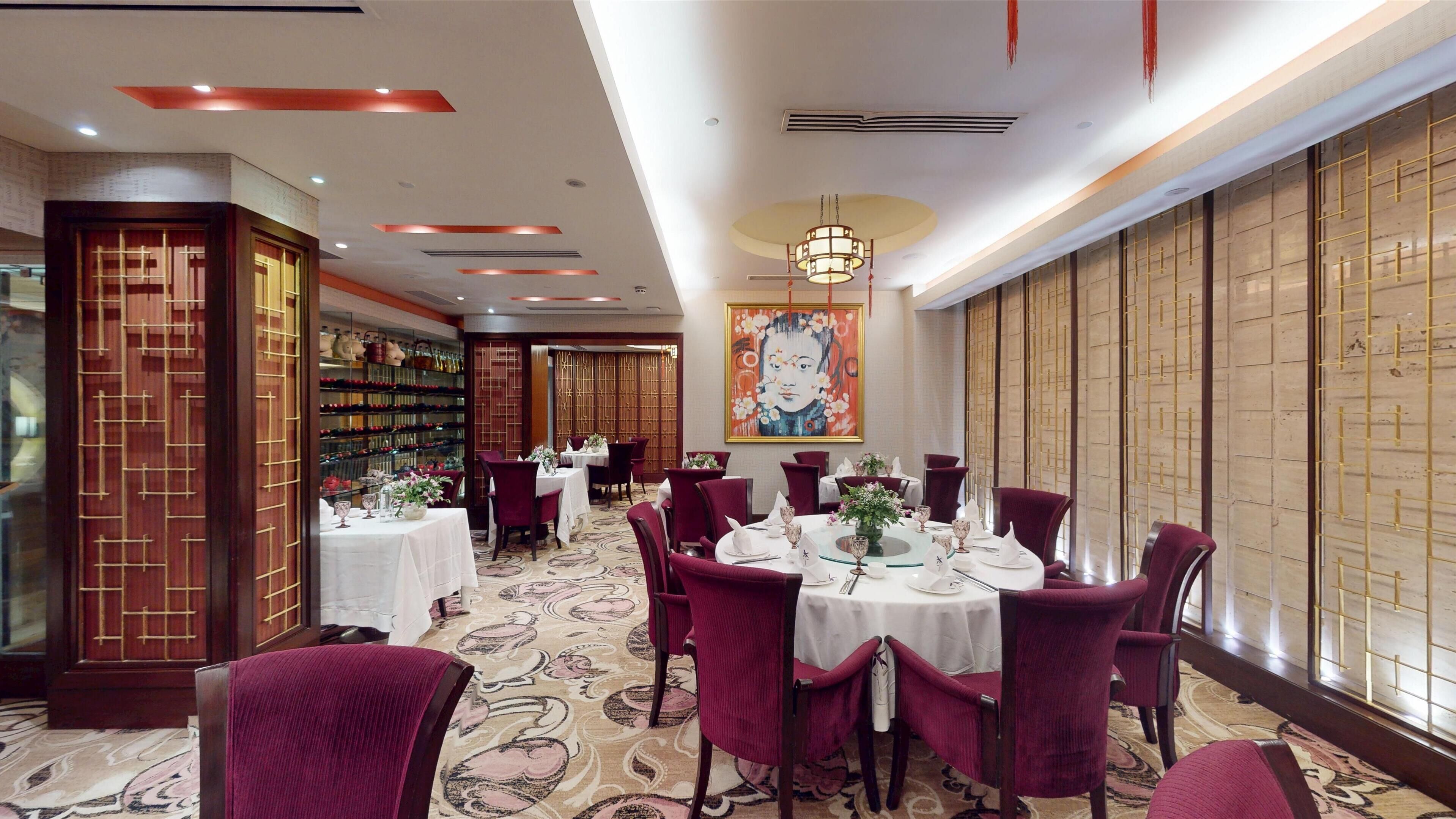 A dining area with round tables, red upholstered chairs, and a patterned carpet.